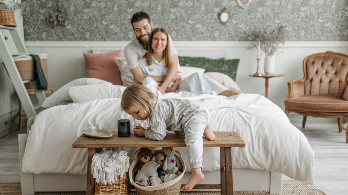 A family enjoying a relaxed morning in a cozy bedroom with a toddler playing.