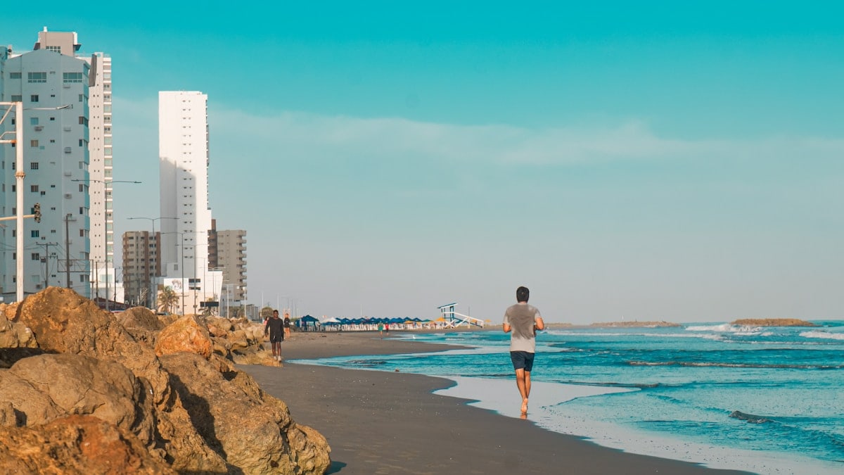 A man walking along a beach next to tall buildings